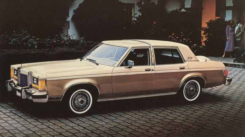 Front 3/4 view of golden Lincoln Versailles on cobbles in a residential setting