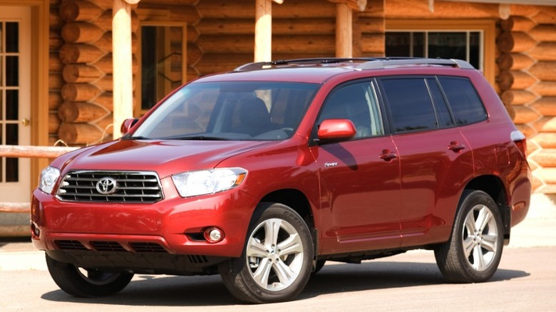 Red 2010 Toyota Highlander parked in front of a log cabin.