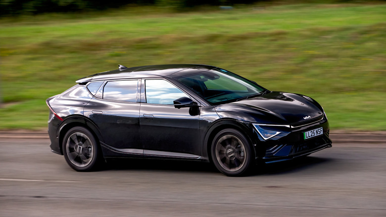A black Kia EV6 GT Line trim electric vehicle driving down a small, winding road with grass on both sides.