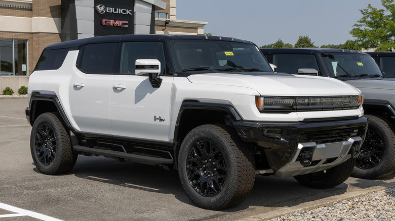 A white GMC Hummer EV first-generation SUV parked in front of a red brick building.