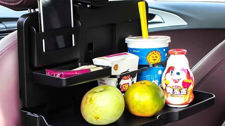 A car tray attached to the driver's seat containing beverage and chips
