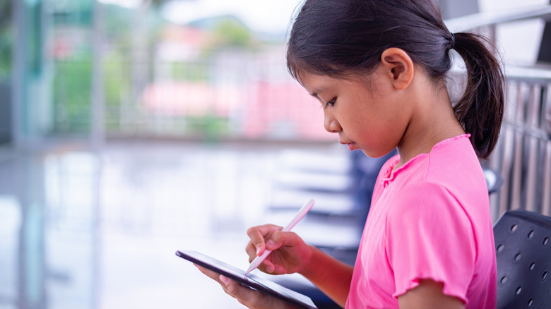 A young girl in a pink shirt using a stylus on a tablet