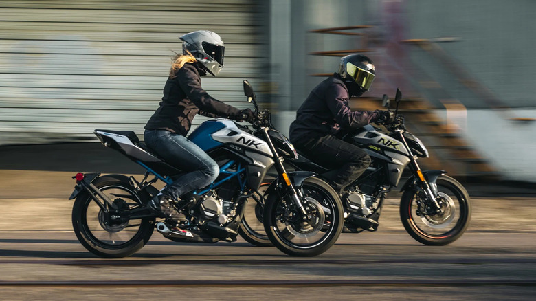 Two riders, each in full riding gear, moving at speed down a road on two CFmoto 300NK naked bikes.