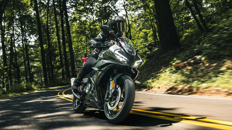 A rider in full gear with a helmet zooming down a forested road on a black CFmoto 300SS.