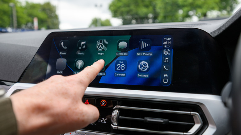 A person interacting with Apple CarPlay on a car's central screen.