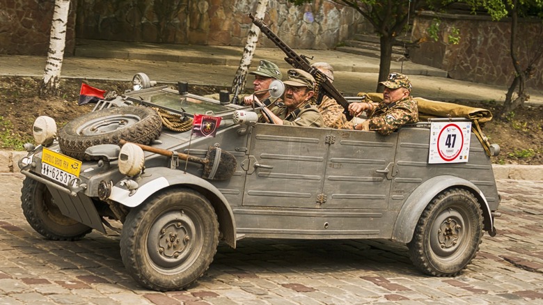 Four men wearing period-correct German uniforms occupy adunkelgrau (field grey)  Kübelwagen Type 82.