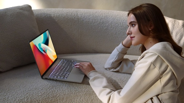 Woman sits on floor with ASUS Zenbook A14 on couch