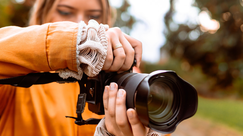 A woman in an orange jacket using a camera with a large lens