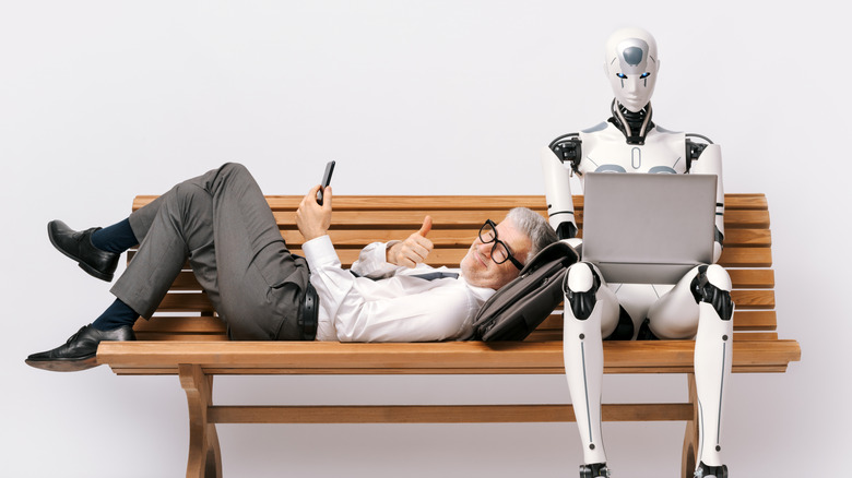 Happy businessman lying on a bench and using a smartphone while an AI robot is working with a laptop and doing his job