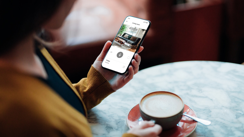 Over the shoulder view of young woman monitoring her home with smart home app