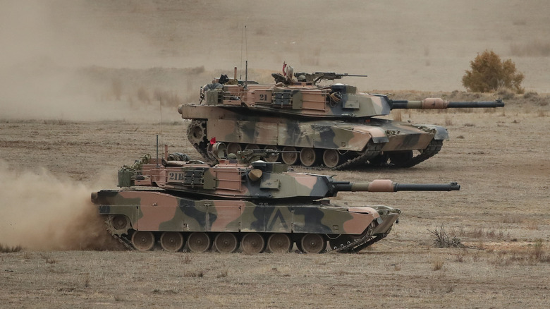 A pair of Abrams tank moving through a dusty field during a military exercise.