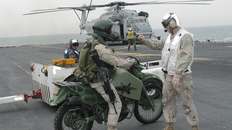A soldier on Kawasaki M1030-M1 with helecopter behind him