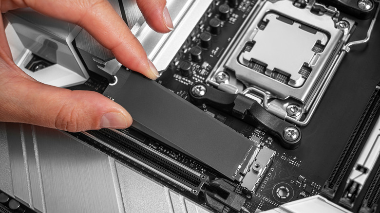 A person is installing an M.2 NVMe SSD into a modern motherboard socket,