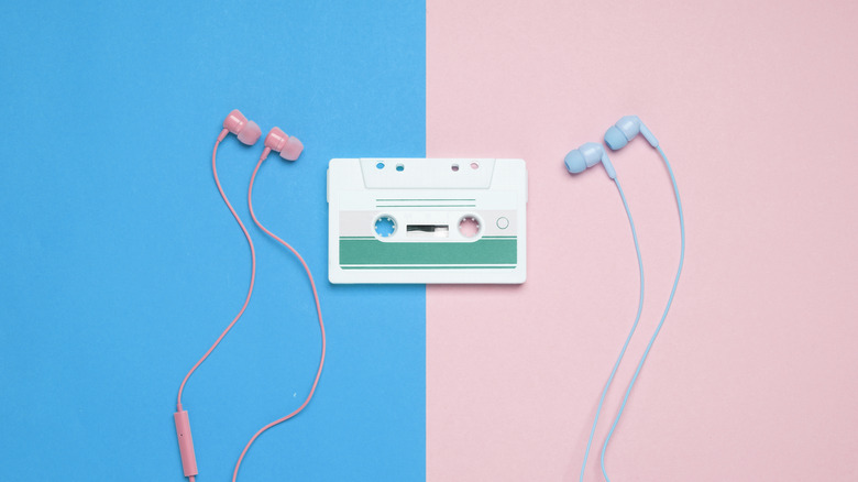 Two pairs of pink and blue wired headphones on contrasting backgrounds with a retro white and green casette tape in the middle.