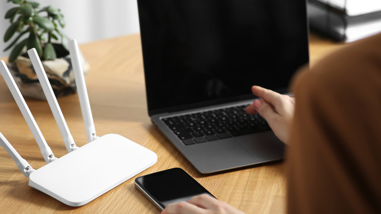 A Wi-Fi router, smartphone, and a laptop placed on a wooden table.