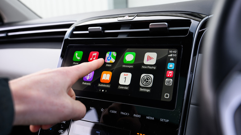 Driver's hand using Apple CarPlay on touchscreen display.