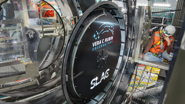 The LSST Camera being installed on the Simonyi Survey Telescope at the Vera C. Rubin Observatory with an engineer looking on.