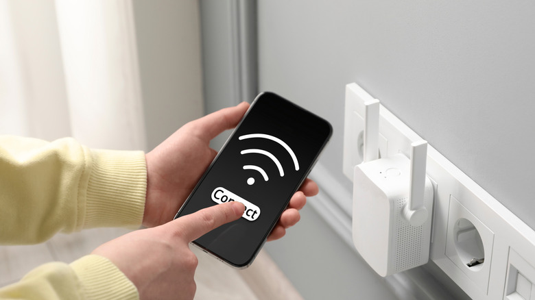 A person with smartphone connecting to internet via wireless repeater indoors