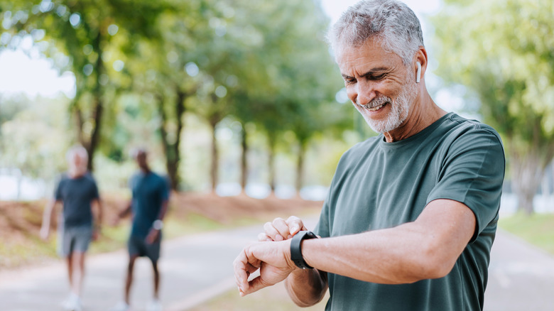 Senior man runner looking at smartwatch outdoor activity.
