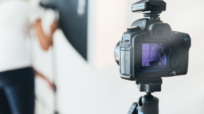 DSLR camera mounted on a tripod as a person adjusts photography studio lights in the background