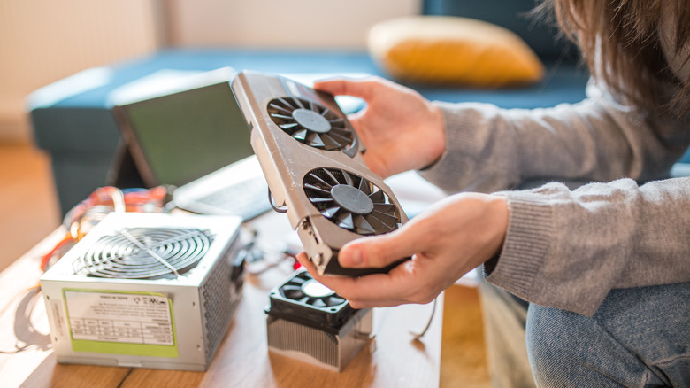 A person holding a small graphics card with other PC components in the background.