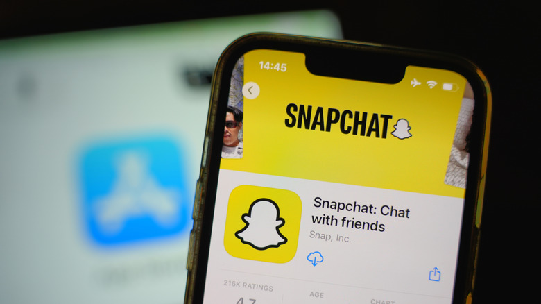 Snapchat's store page shown on a Xiaomi smart phone with the App store on a macbook behind it.