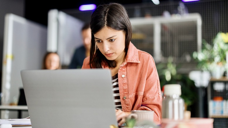 Woman wearing a black and white stripy top and pink jacket using laptop on desk