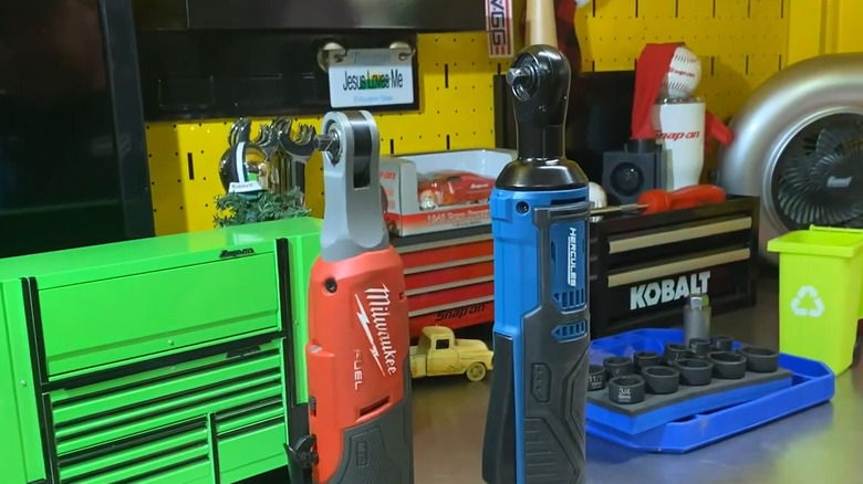 Milwaukee and Hercules electric ratchets upright on steel work table with toolboxes behind