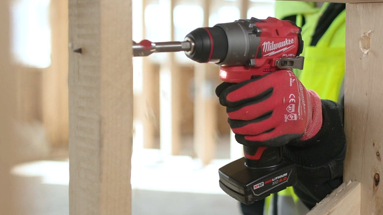 Person using Milwaukee drill with an M12 XC4.0 battery on a wood board