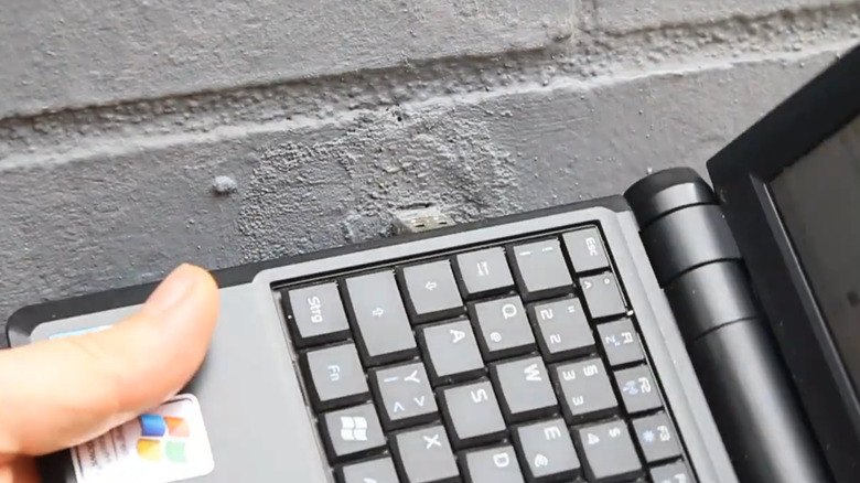 A USB-A drive sticking out of a gray wall with a laptop.