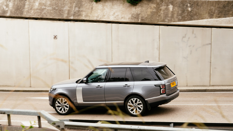 A blue-silver Land Rover Range Rover car driving away from the camera down a city street