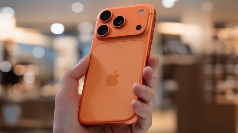 A person holding an orange iPhone 17.
