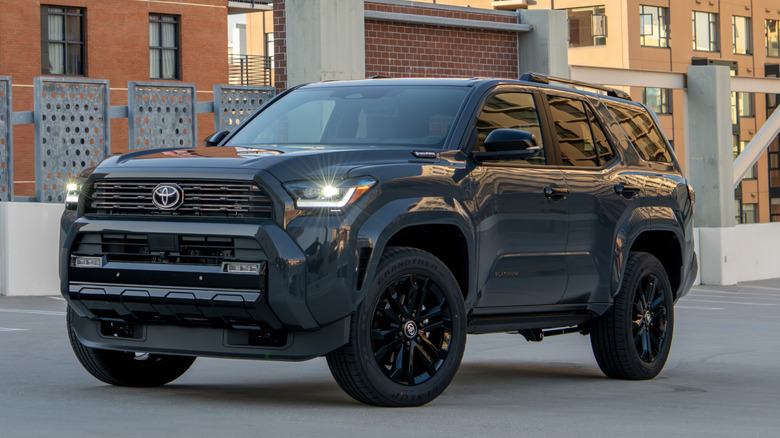 A blocky black SUV parked outside the bays, in the middle of an empty car park, with its lights on, but no-one behind the wheel