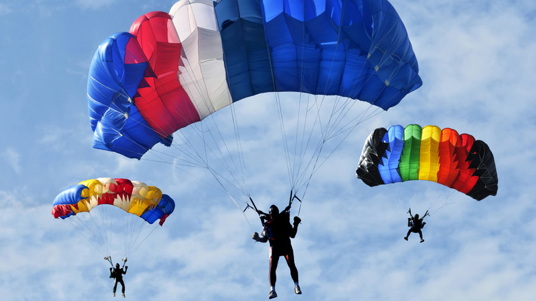 Three skydivers with parachutes deployed against a cloudy blue sky