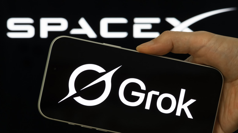 A close-up of a hand holding a smart phone with the Grok logo displayed on it with the SpaceX logo displayed in white in the background
