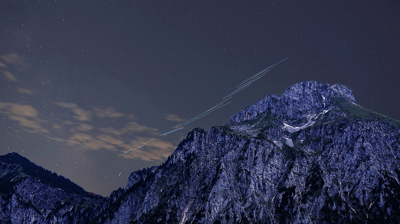 Satellites in the night sky over a dramatic mountain