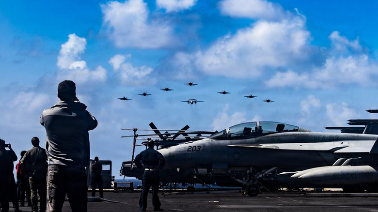 US Navy personnel on deck of USS Gerald Ford aircraft carrier watching ceremonial flyover