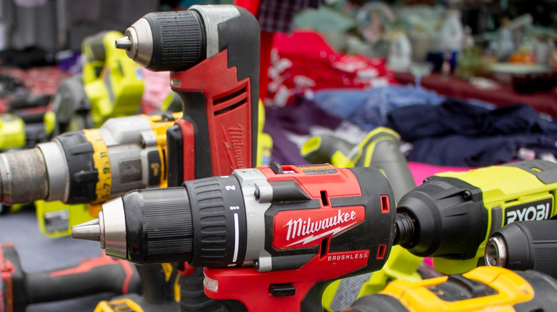 Many drills and drivers from various brands on a table, including Milwaukee and Ryobi.