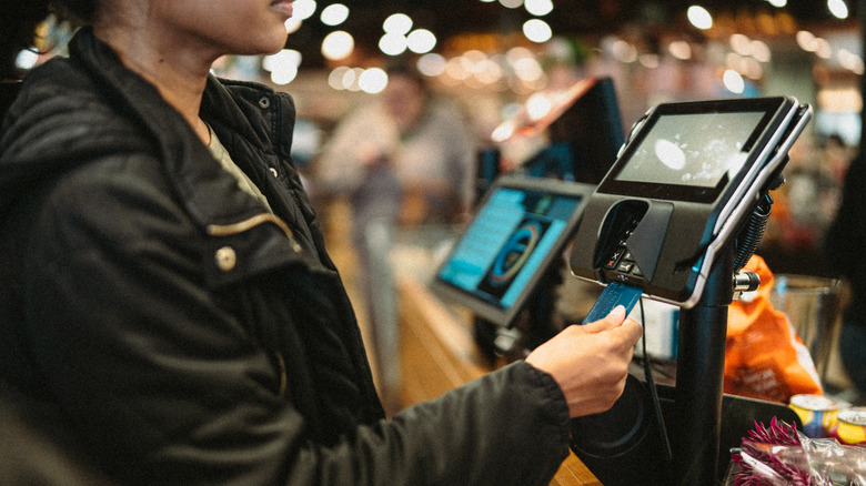 A woman using a credit card to tap-to-pay when buying items at the grocery store