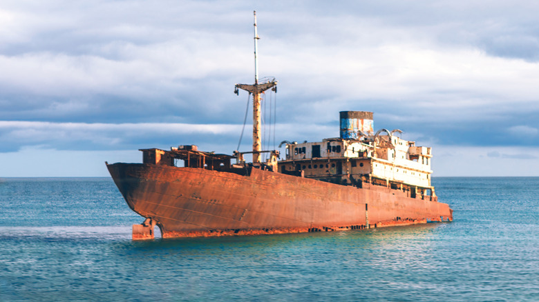Rusty abandoned ship stranded in calm turquoise sea under dramatic cloudy sky