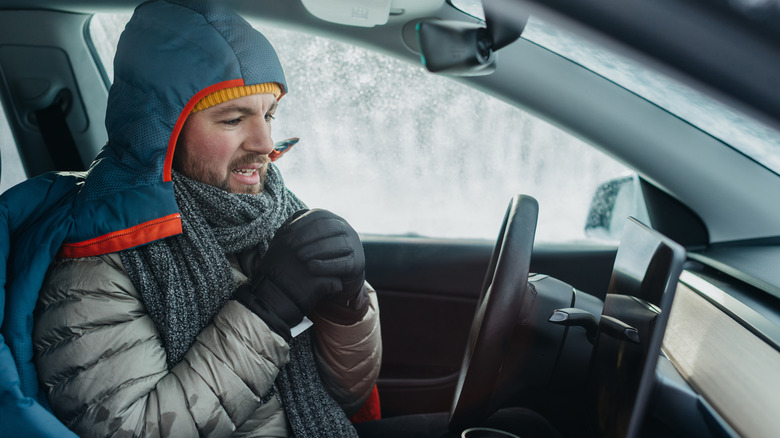 Man wearing warm clothes and gloves trying to get warm inside an electric car during cold winter conditions
