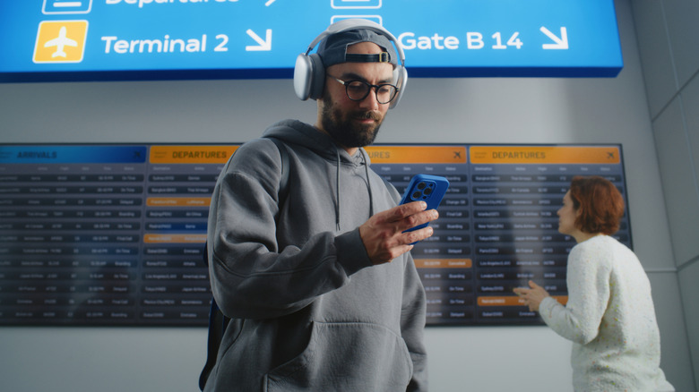 Man using phone with headphones in airport