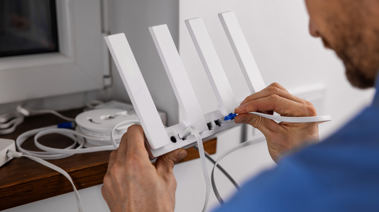 A man trying to connect ethernet cable to a Wi-Fi router at home