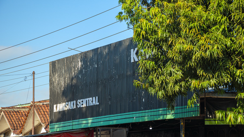 A store with Kawasaki Sentral in white lettering on the metal frontage of the store with a tree in the foreground.