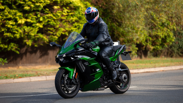 A man in full gear riding a dark green and black Kawasaki Ninja H2 SX model down a road at speed.