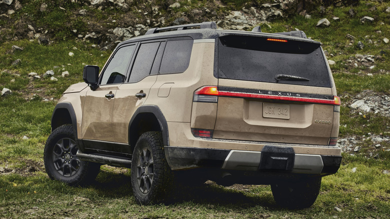 Rear 3/4 view of gold Lexus GX 550 on hillside with rocks and grass