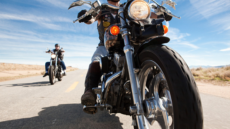 Two men riding motorcycles on a dusty road.