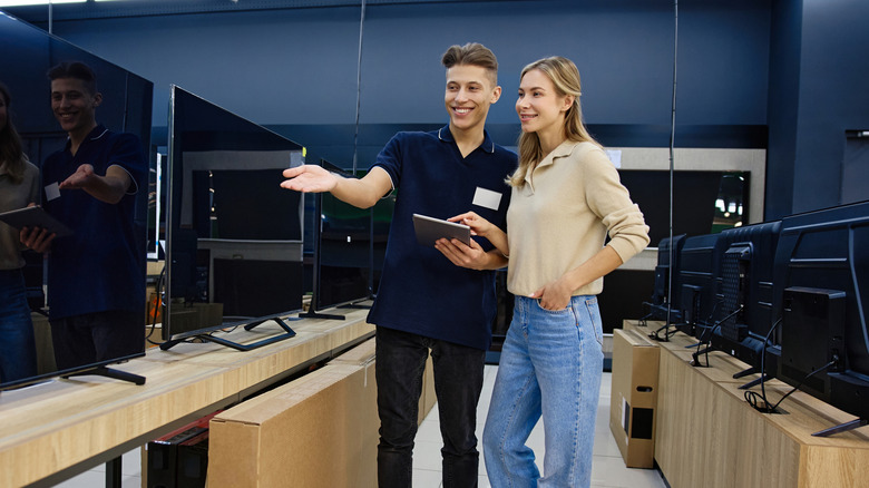 Two people looking at televisions in a store showroom.
