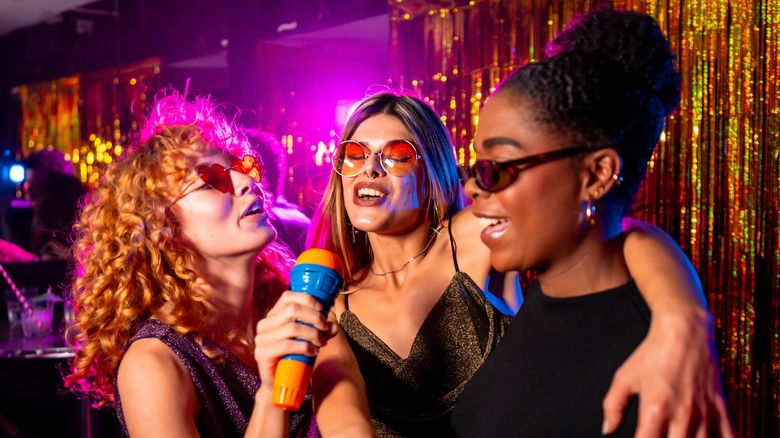 Three women singing into a colorful microphone