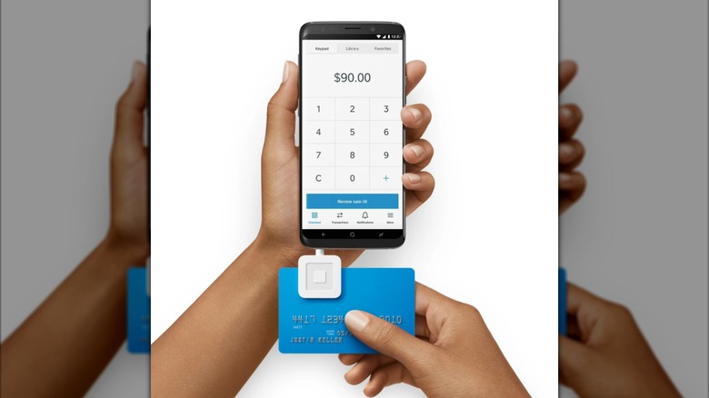 A Square headphone jack EMV chip card reader plugged into a smartphone.